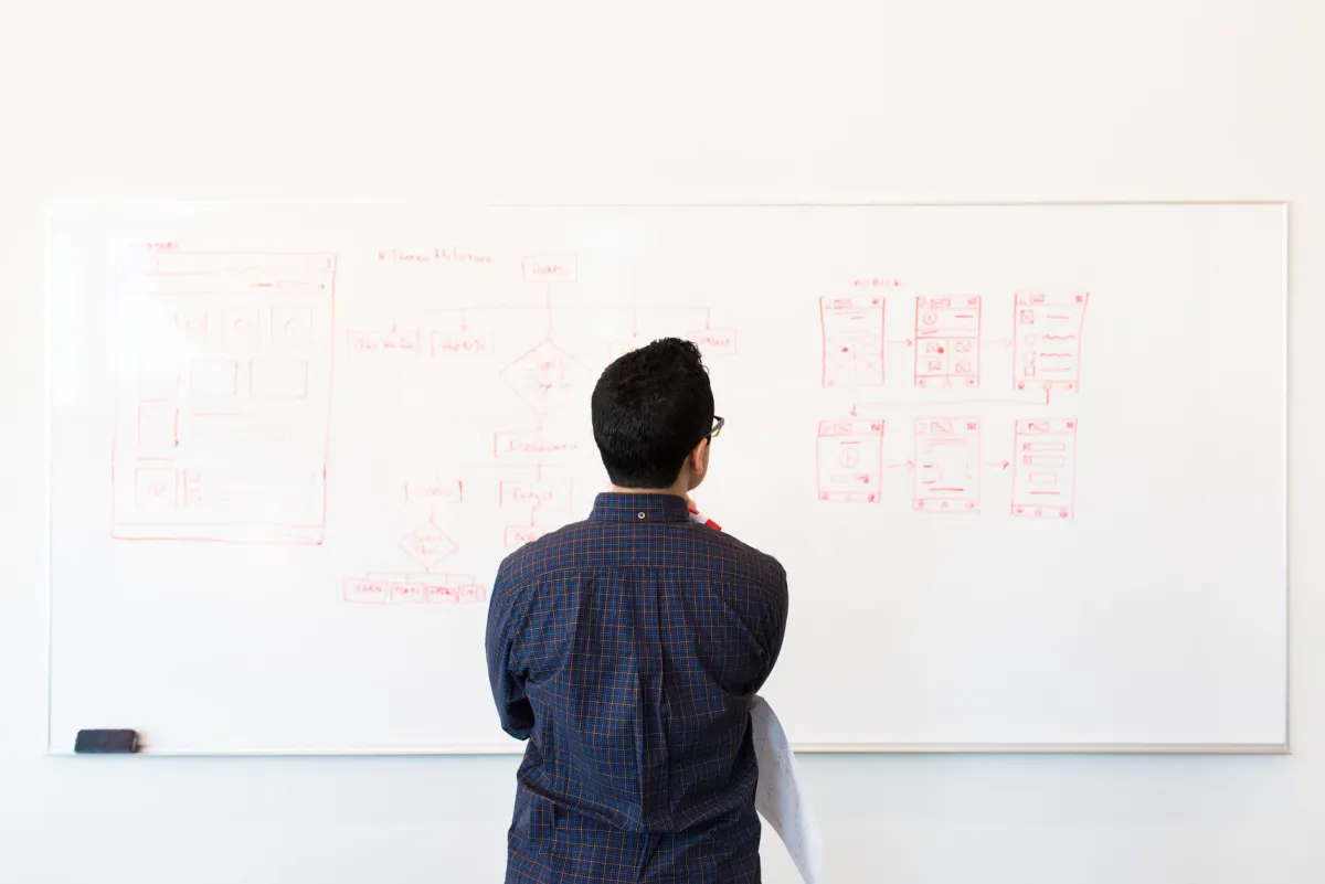 A developer reviewing written workflow notes beside a computer while planning an automated software process.