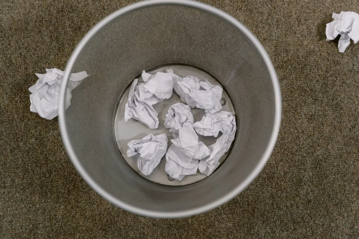 A paper shredder on an office floor with strips of shredded paper in its bin.