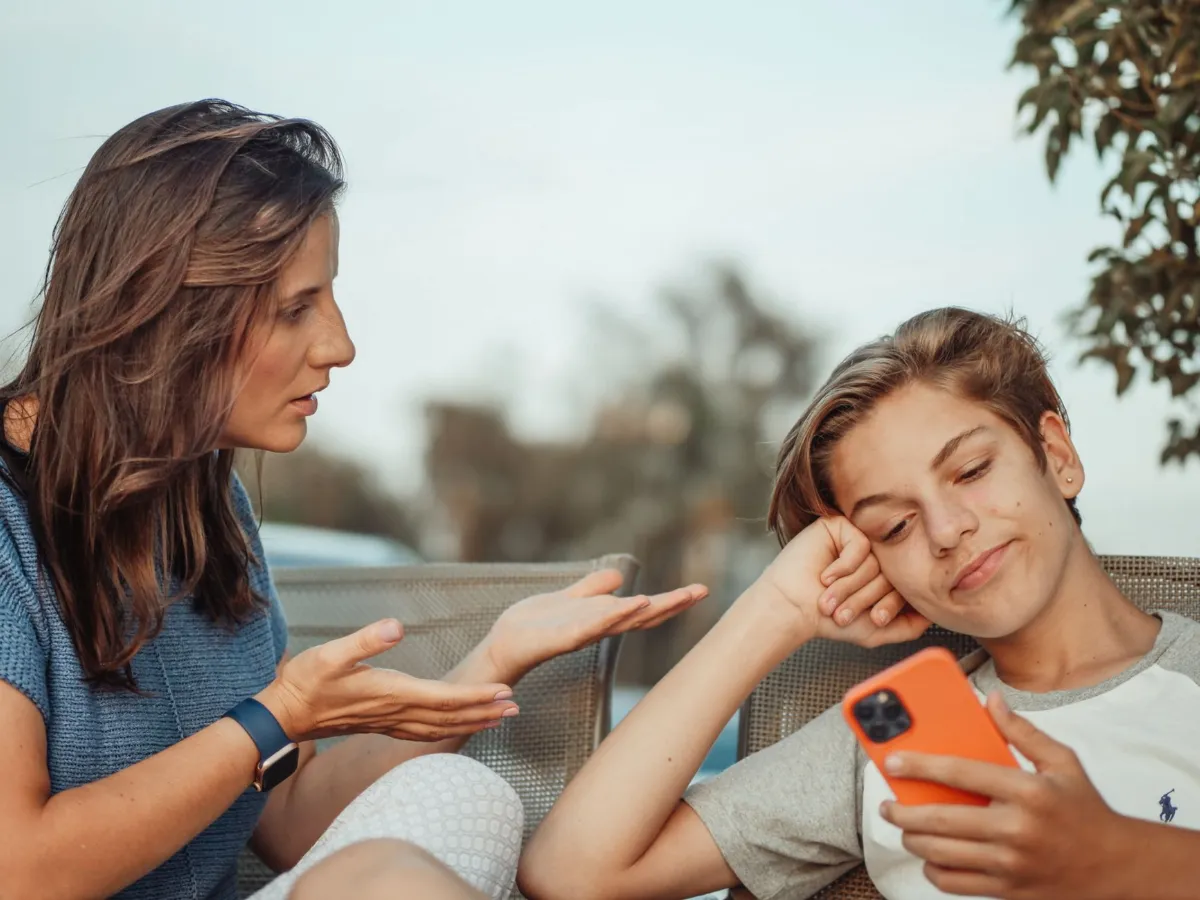 A parent and a teenager sit together on a sofa looking at a smartphone.