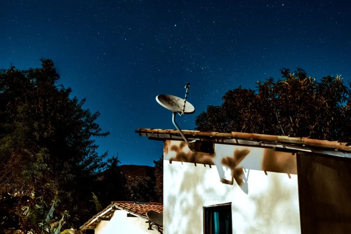 A satellite broadband terminal installed outside a rural property surrounded by open countryside.